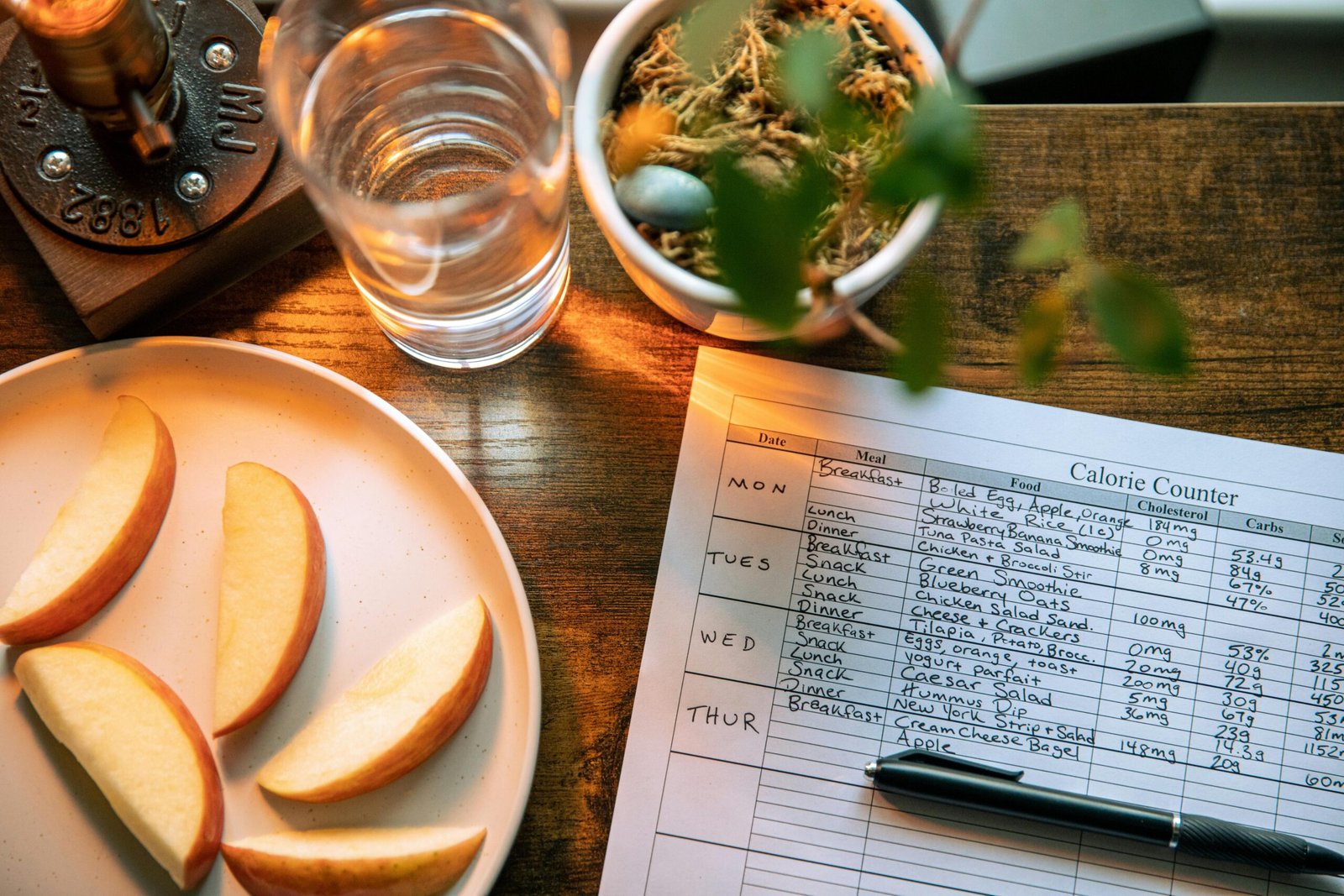 Home Top view of apple slices, water, and a calorie counter sheet on a wooden table promoting a healthy lifestyle.