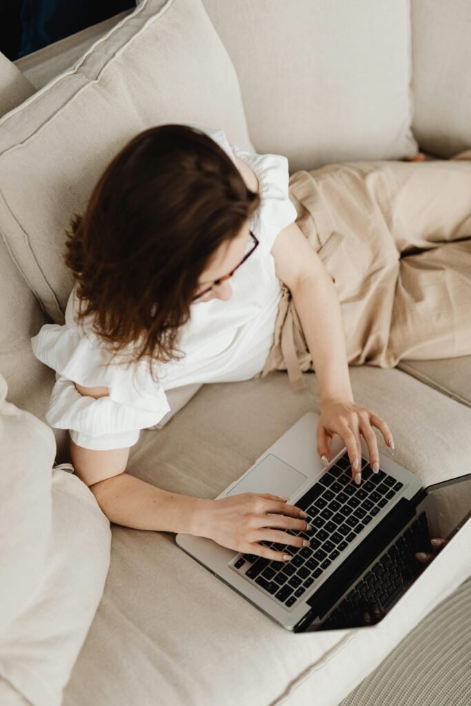 Are Longer Airbnb Stays Better? 5 Benefits for Hosts (And When to Think Twice) Woman comfortably using a laptop on a beige sofa indoors, viewed from above.