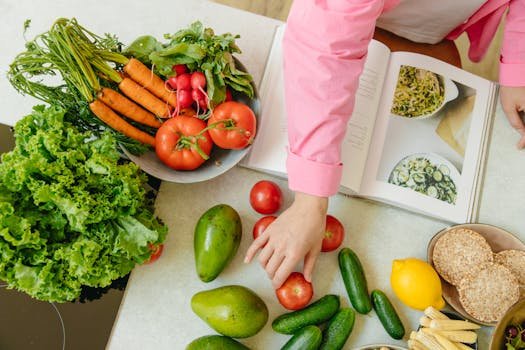 Home Top view of fresh vegetables and hands arranging them with a recipe book, promoting healthy eating.